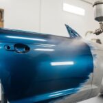 HVLP automotive paint sprayer applying smooth metallic paint to car panel in garage